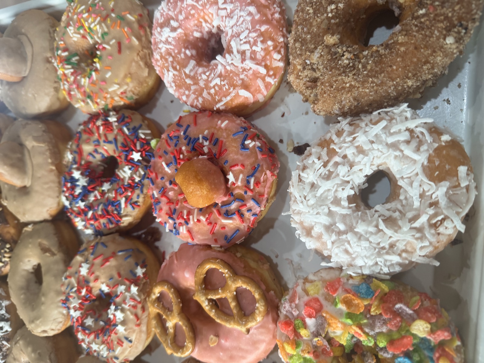 Rows of frosted donuts with sprinkles, coconut and pretzels